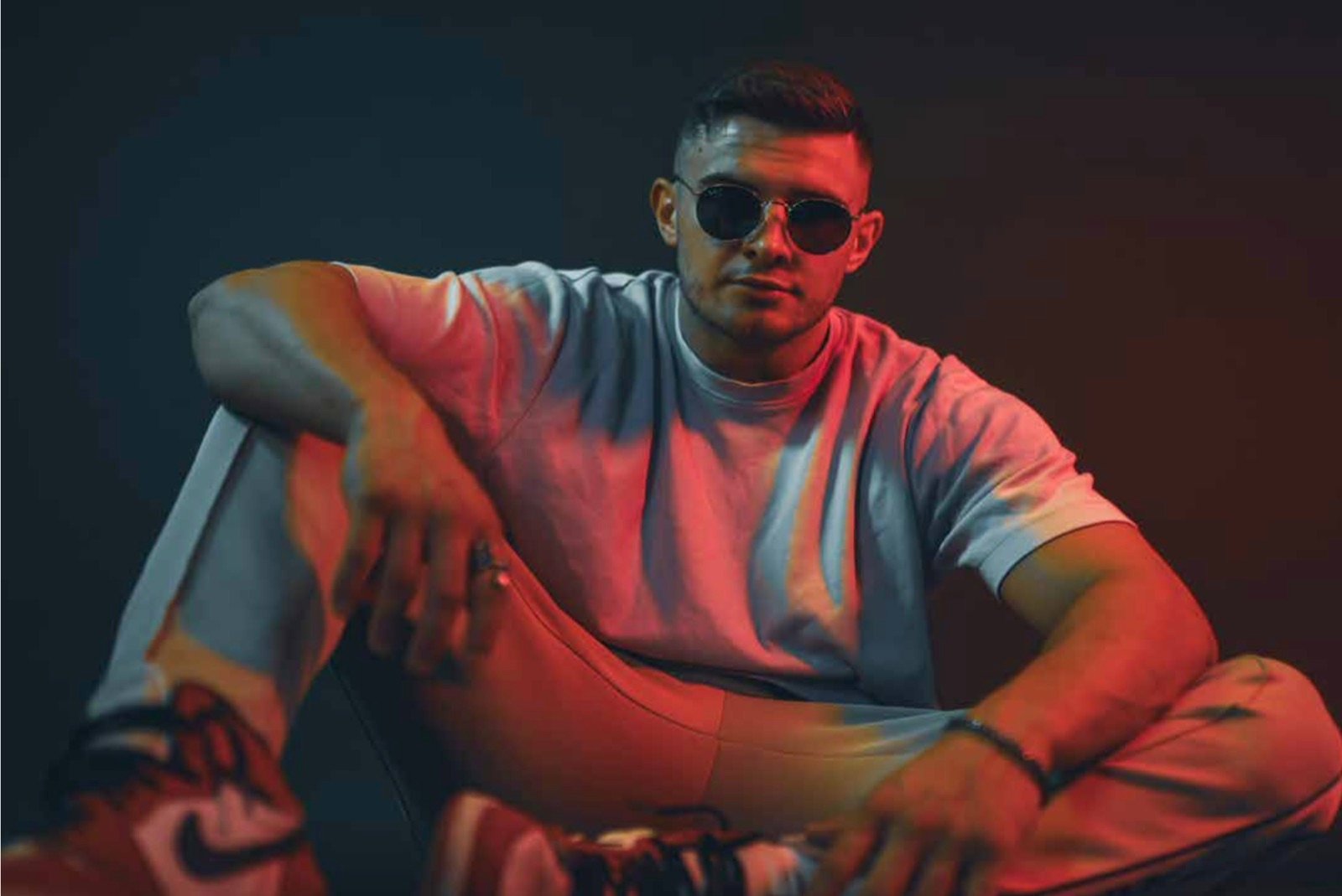 Farbportrait eines sitzenden Mannes mit Sonnenbrille in rotem und blauem Licht